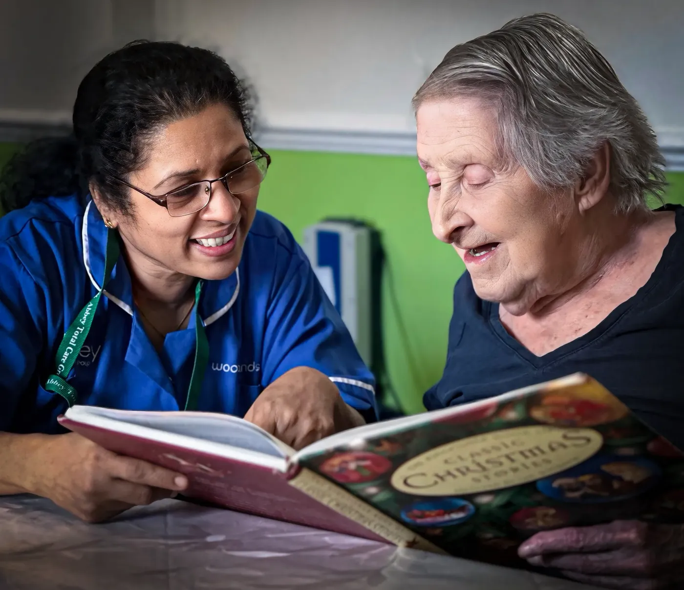 A carer reading a Christmas book with a resident at Woodlands Total Care Nursing Home, Ilford
