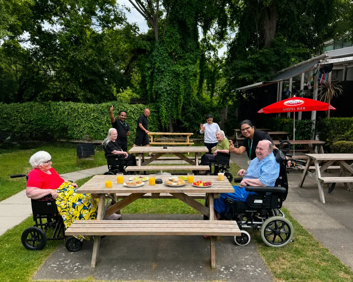 Residents and staff at picnic tables in the sunshine during a pub lunch with Woodlands Total Care Nursing Home